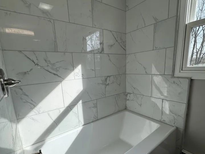 Full bathroom with new tub and marble-look tile surround