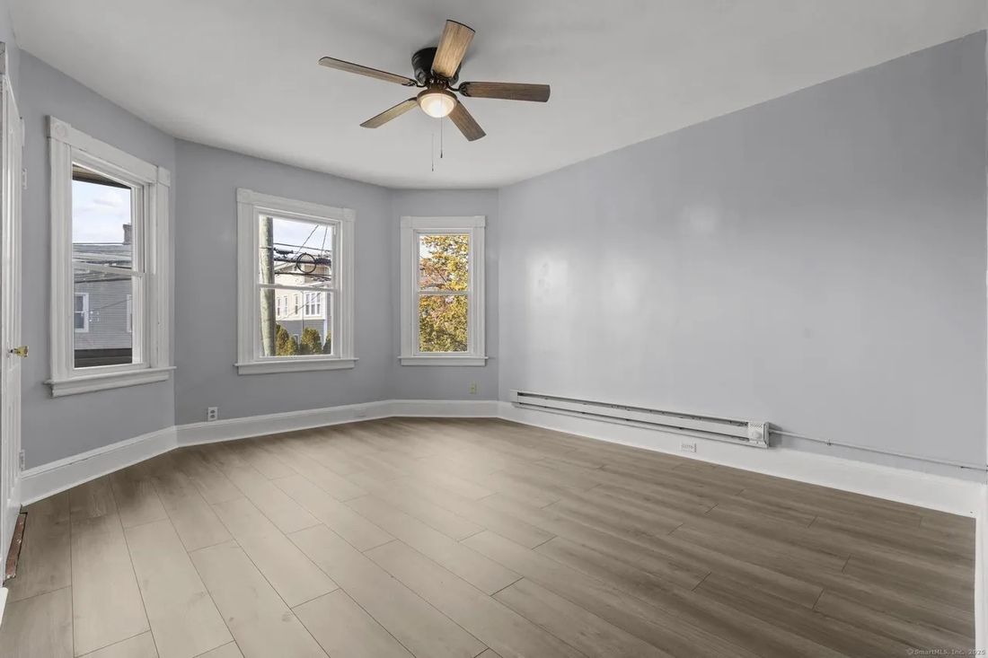 Living room in a New Britain triplex unit with bay window, ceiling fan and new luxury vinyl plank flooring