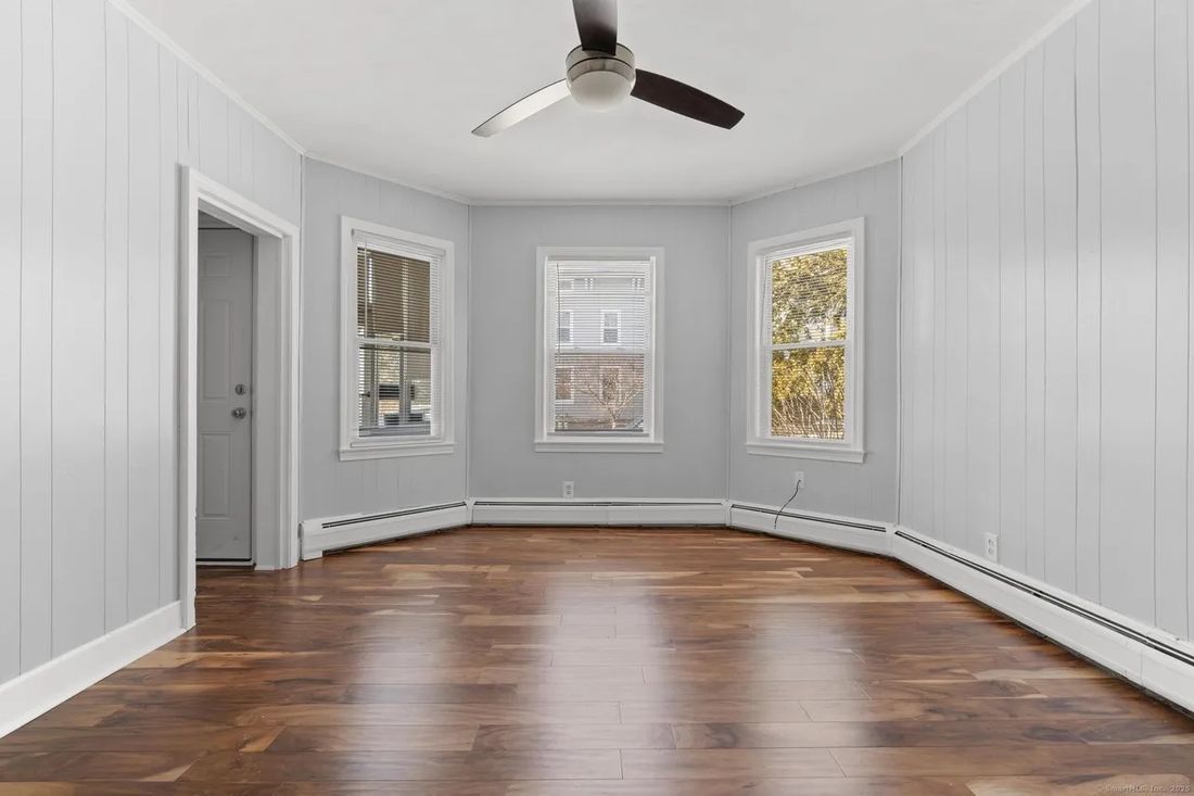 Third-floor living space with restored hardwood floors and bay window in the New Britain triplex
